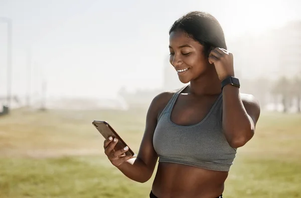フィットネスポッドキャストのための黒人女性 音楽イヤフォンや携帯電話 スポーツ草のフィールド上の運動動機やトレーニングラジオ 5Gアプリでアスリートやワークアウトの健康データのための笑顔 幸せとモバイル技術 — ストック写真