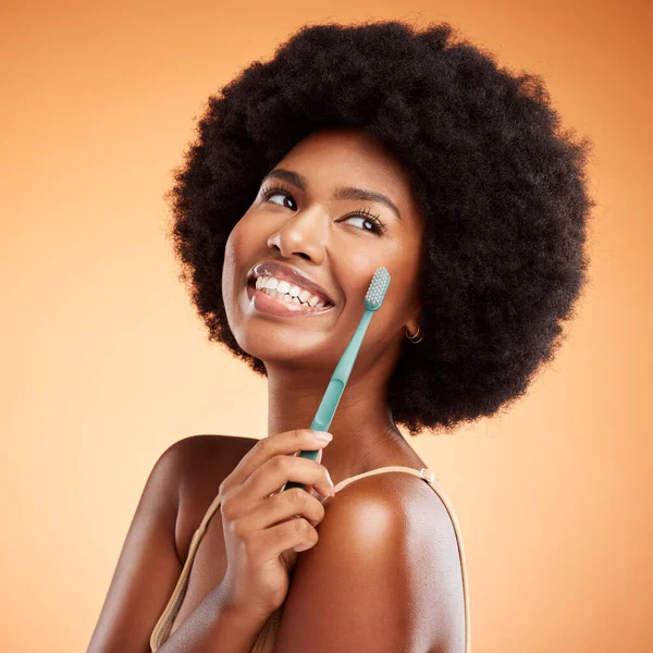 Brushing teeth, woman skincare and dental wellness, health or cleaning cosmetics on orange studio background. Happy young african model toothpaste, toothbrush and smile with afro hair, face and mouth.