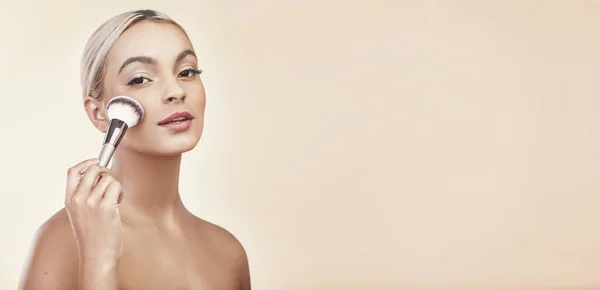 A little contouring does the trick. Studio shot of a beautiful young woman holding a make-up brush against her face