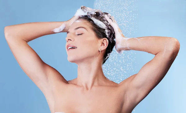 Theres nothing more refreshing than that squeaky clean feeling. Studio shot of a young woman washing her hair with shampoo while taking a shower against a blue background