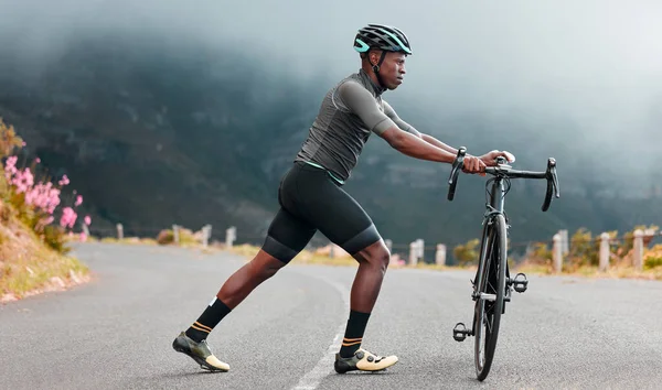 Stretching legs, fitness and man cycling on a road with a bike in the mountains for cardio, travel and sports workout in nature. Athlete doing a warm up before training on a bicycle in the street.