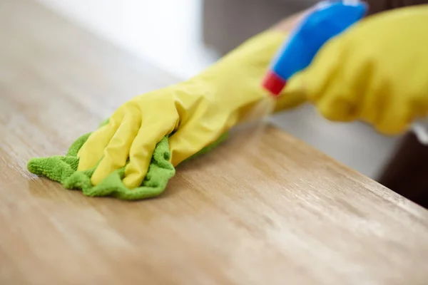 You never know where germ might be lurking. a woman wearing gloves and holding a spray bottle while cleaning a wooden surface at home