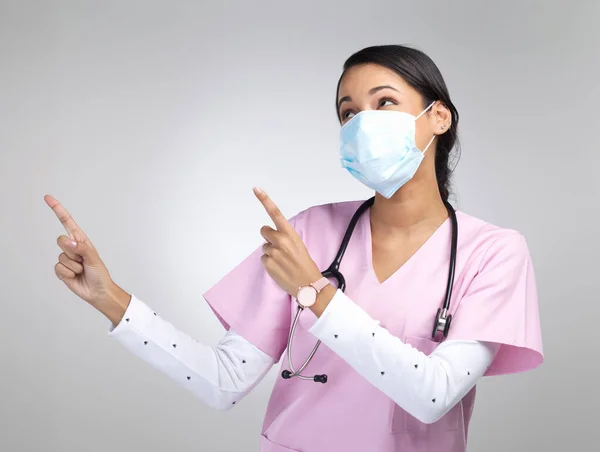 どこの医師によって承認 マスクをつけてスタジオのコピースペースを指差す魅力的な若い女性医療従事者です — ストック写真