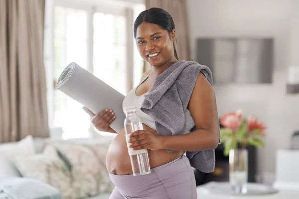 Maintaining healthy pregnancy habits has many benefits. a pregnant woman holding a water bottle and yoga mat at home
