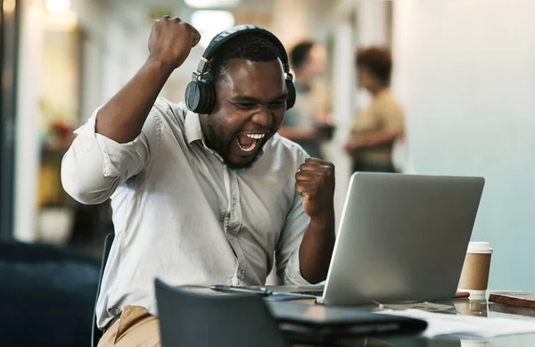 We just got the biggest client of the year. a young businessman sitting and celebrating an achievement while wearing headphones and using his laptop