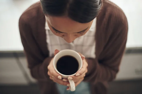 暗く落ち着いたカップをお楽しみください 自宅でコーヒーを飲む若い女性の高角度ショット — ストック写真