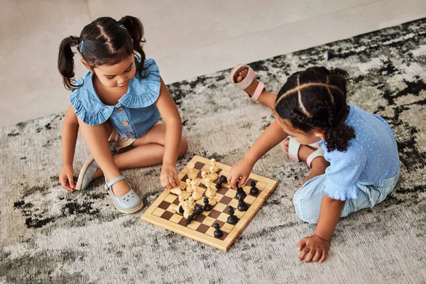 Girl children, knowledge fun and chess game on a living room carpet for home education. Kids in a household for brain development growth, youth problem solving and strategy playing on floor and rug.