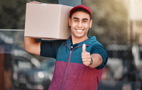 Portrait, box and delivery worker with thumbs up gesture and a big smile carrying cargo, stock or a package. Happy delivery man with a thumb up holding a cardboard packaging or mail post outdoors.