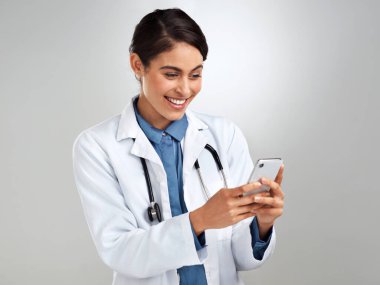 Doktorların çevrimiçi ve dinliyor. Genç bir doktorun gri arka planda akıllı telefon kullanırken çekilmiş bir fotoğrafı.