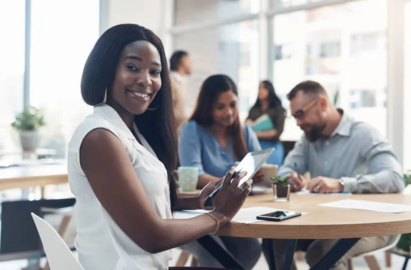 Im on the correct career path. Cropped portrait of an attractive young businesswoman sitting and using a tablet while her coworkers work behind her