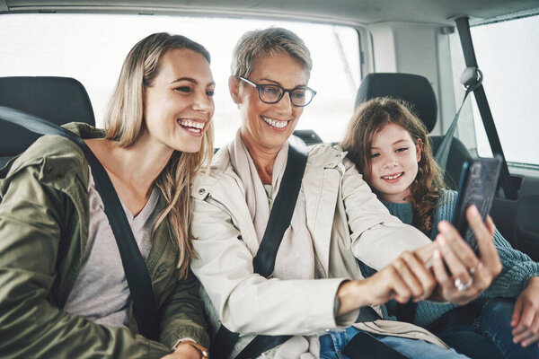 Phone, selfie and happy family in a car for a road trip driving or traveling to a holiday vacation adventure together. Grandma, mother and excited girl or child enjoy pictures for a fun weekend.