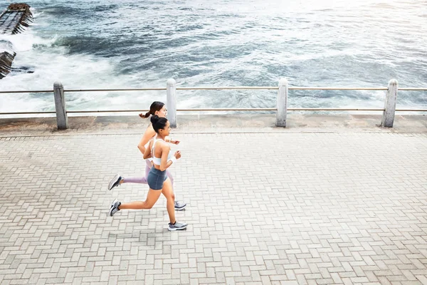 Fitness friends, woman and running for exercise above in workout, training and cardio in South Africa. Active women in sports run together by the ocean in sea point for healthy exercising in nature.