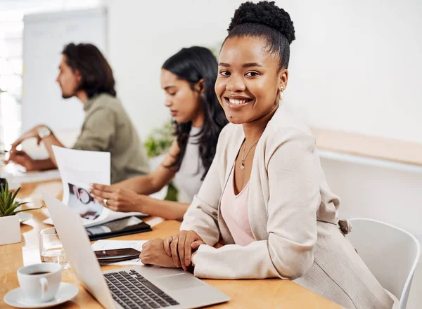 Its here where we work our magic as a team. Portrait of a young businesswoman sitting in an office with her colleagues in the background