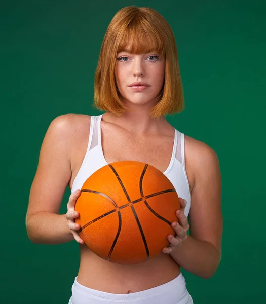 我向你挑战一位年轻貌美的女运动员独自站在演播室里 拿着一个绿色背景的篮球 — 图库照片
