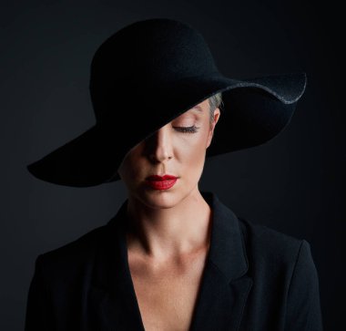 Elegance is a question of personality, more than ones clothing. Studio shot of a beautiful mature woman wearing a hat and posing against a dark background clipart
