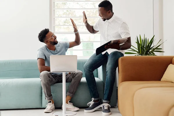 Thank for the help. Full length shot of two handsome businessmen giving each other a high five while working together in the office