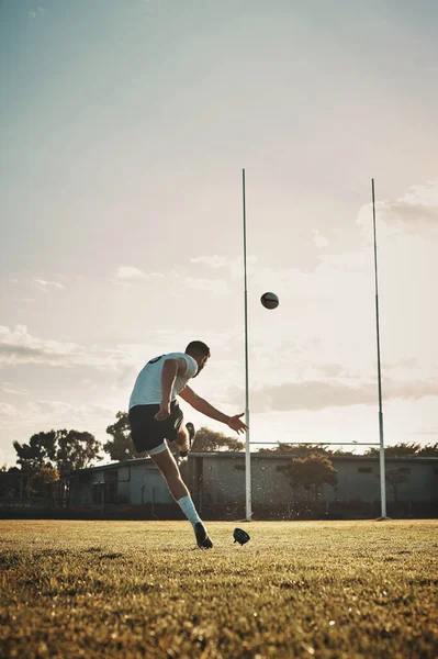 Such great kicking skills. Full length shot of a handsome young rugby player kicking a ball on the field during the day