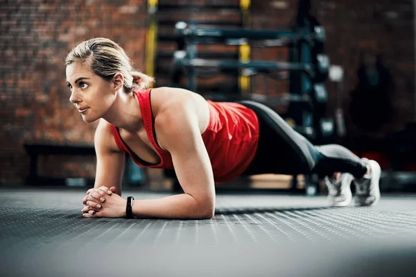 Holding it for as long as she can. Full length shot of an attractive young female athlete planking in the gym