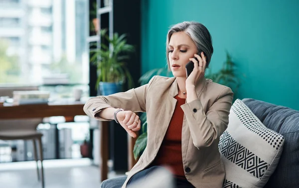 I better get moving. an attractive mature businesswoman sitting alone and talking on her cellphone in her home office