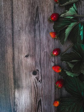 Ahşap arka planda yeşil yapraklı çilekler.