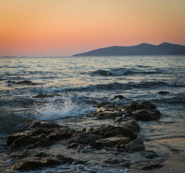 Güneşin dağların ardında battığı, altın saatinde kayaların ve plajların üzerinde uzun bir deniz manzarası..