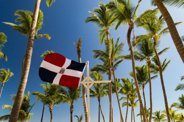 Dominik Cumhuriyeti bayrağı rüzgarda dalgalanıyor palmiye ağaçları arasında ve Karayipler 'de mavi bir gökyüzüne karşı..