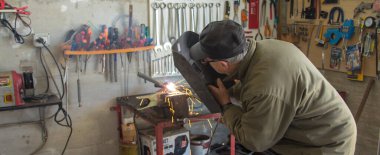 Kıdemli demirci mekanik parçaları kaynak yaparken atölyesinde. Yatay Pankart 