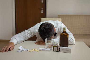 Anksiyete ilaçları, antidepresanlar, sakinleştiriciler ve alkol gibi psikotropik ilaçları kullandıktan sonra kafası masada dinlenen bir adam. Maddelerin sorununu ve bağımlılığını temsil eden görüntü