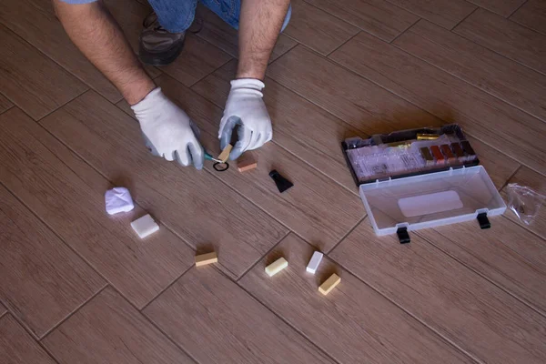 Image of the hands of a handyman repairing a splinter on a tile on the floor at home