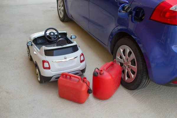Picture of a small electric toy car and a real car with the fuel cap open and without gasoline with two empty canisters. Reference to the growing increase in the cost of fuels