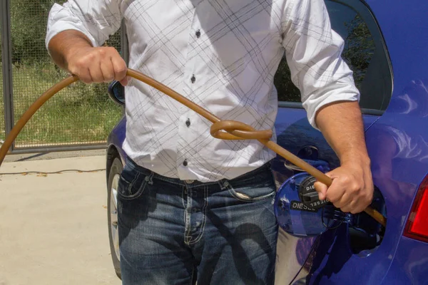 Man tying a knot to a tube of tires that is in the tank of the car. Reference to the constant increase in fuel prices.