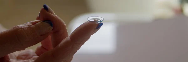 Image of a woman\'s hand holding a contact lens on her finger. Horizontal banner