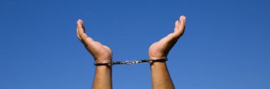 Image of a man's hands facing the sky with handcuffs on his wrists after arrest. Reference to freedom. Horizontal banner