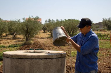 Picture of a desperate farmer with an empty bucket because there is no more water in the well. Reference to climate change and drought in agriculture