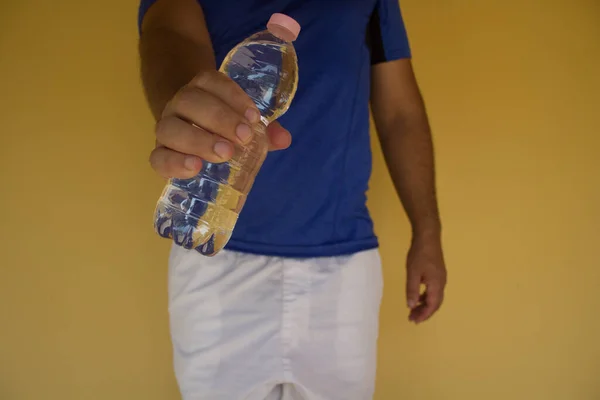 Image of a man's hand holding a bottle of water after playing sports. Reference to the importance of hydration after sport and in the summer and hot periods