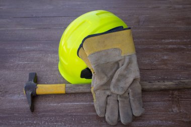Image of a mason's hammer, hard hat and work gloves. Reference to manual work and accidents at work