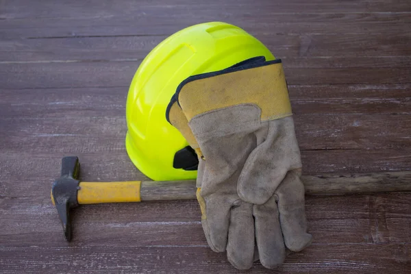 Image of a mason\'s hammer, hard hat and work gloves. Reference to manual work and accidents at work