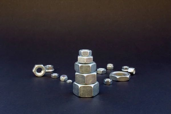 Image of a pyramid of nuts with a black background and various bolts