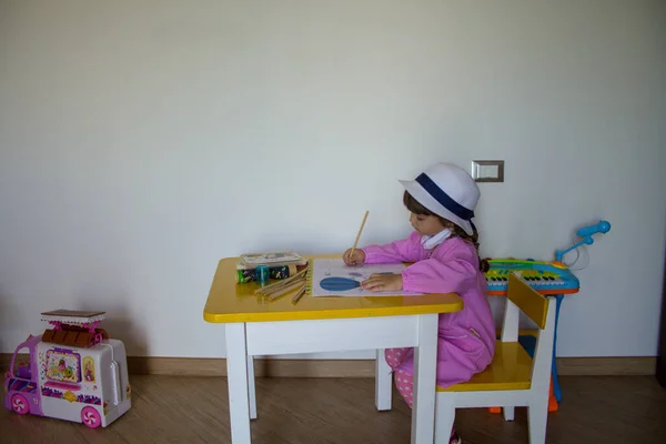 Adorable little girl with pink hat and apron playing with pencil colors in a notebook. Back to school and first day of kindergarten