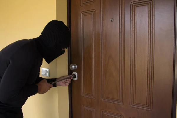 一个小偷穿着一身黑色衣服 头戴巴拉克拉瓦 试图用大螺丝刀撬锁房门 经济危机导致的入室盗窃不断增加 — 图库照片