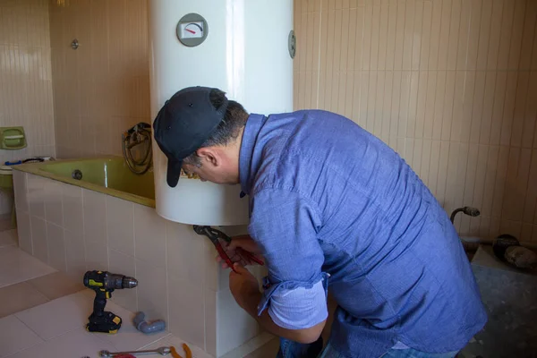 Plumber in the bathroom of a house who with his work tools repairs an electric water heater. Installation of a boiler in the bathroom, do-it-yourself work.
