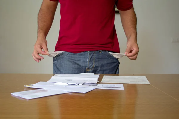 Image of a man with his trouser pockets turned inside out in front of some electricity and gas bills. Reference to the increase in the cost of bills due to the global crisis