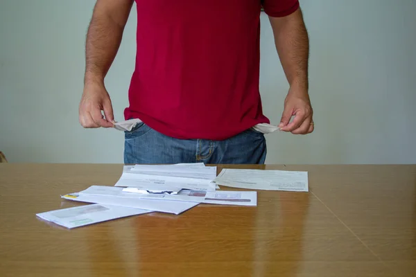 Image of a man with his trouser pockets turned inside out in front of some electricity and gas bills. Reference to the increase in the cost of bills due to the global crisis