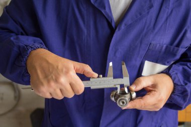 Atölyesinde bir arabanın çaprazını kalibreyle ölçen bir tamircinin elleri. Hassasiyet mekaniği.