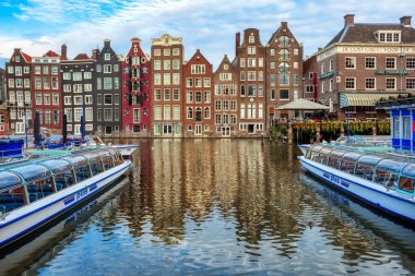 Amsterdam, Hollanda - 14 Temmuz 2020: Amsterdam 'da Damrak Kanalı' ndaki geleneksel tuğlalı evlerin önündeki botlar. Tekne gezileri Amsterdam 'da popüler bir turistik eğlencedir..