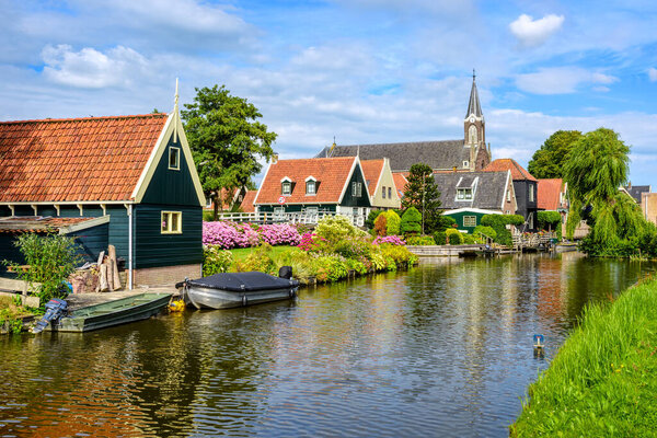 Picturesque idyllic De Rijp village in North Holland, Netherlands, view of characteristic wooden houses with red tiled roofs and flower beds and the church reflecting in a river
