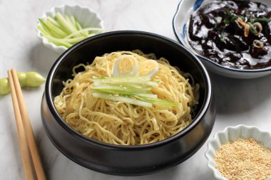 Jajangmyeon ya da JJajangmyeon Kore Noddle yanında salatalık ve susam tohumu ile servis edilir.