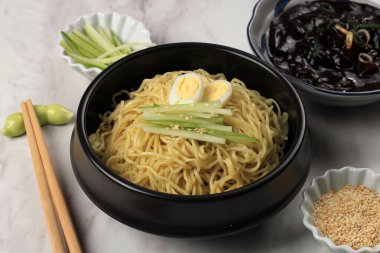 Jajangmyeon ya da JJajangmyeon Kore Noddle yanında salatalık ve susam tohumu ile servis edilir.