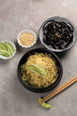 Jajangmyeon ya da JJajangmyeon Kore Noddle yanında salatalık ve susam tohumu ile servis edilir.