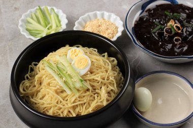 Jajangmyeon ya da JJajangmyeon Kore Noddle yanında salatalık ve susam tohumu ile servis edilir.